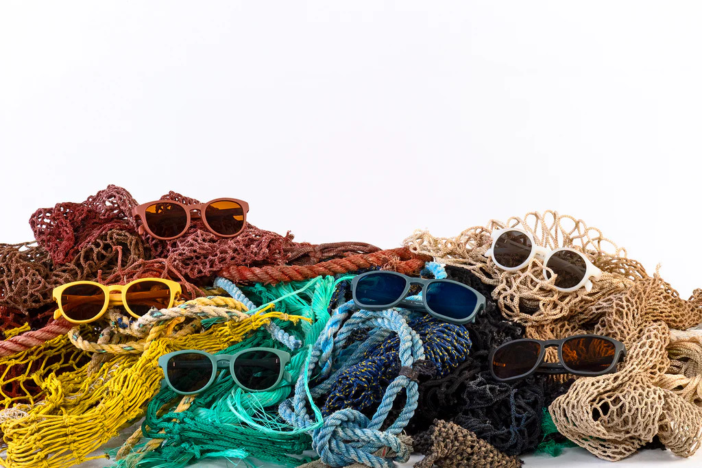 Multiple brightly colored pairs of Karun sunglasses displayed in tangles of matching colored nets, against a white background.